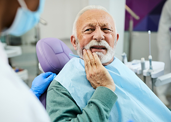 Senior man holding his cheek and wincing while talking to dentist