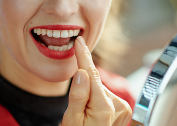 Woman with red lipstick looking at her teeth in mirror