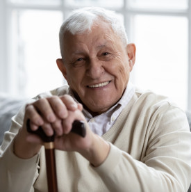 Smiling senior man sitting on a couch and resting his hands on his cane