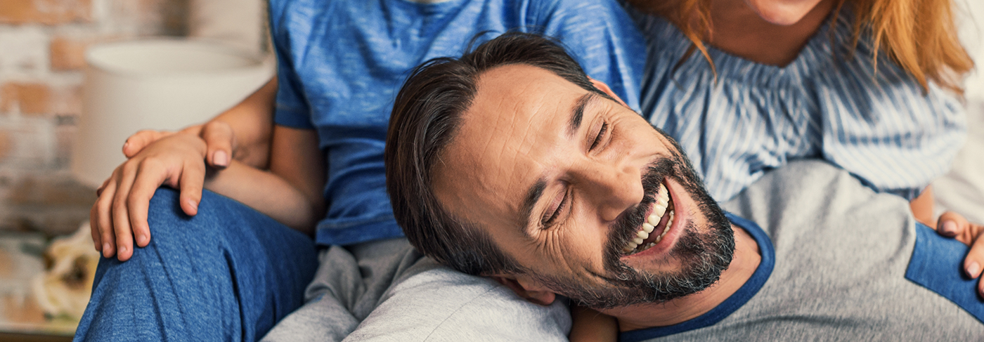 Man relaxing on couch with his family and smiling with dental implants in Londonderry