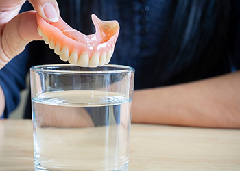 Person soaking their denture in a glass of water