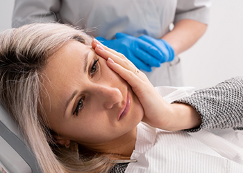 Woman holding her cheek in pain while looking at her emergency dentist