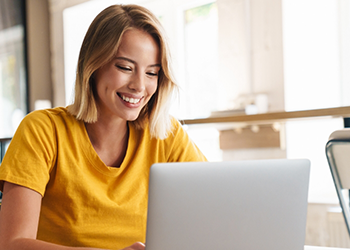 Woman in yellow shirt smiling while using her laptop