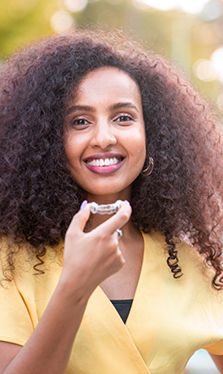 Smiling woman holding an Invisalign clear aligner