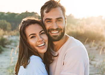 Man and woman smiling and hugging outdoors in late afternoon sun