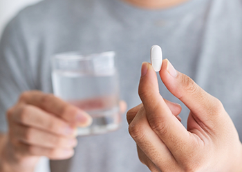 Person holding a white pill and a glass of water