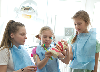 Three kids in dental office looking at a model of the teeth