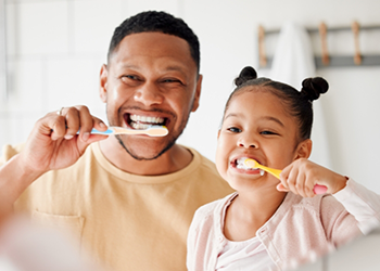 Father and young daughter brushing their teeth together